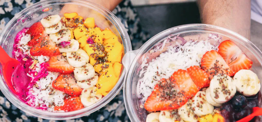 Two açaí bowls garnished with coconut, strawberries, and bananas.