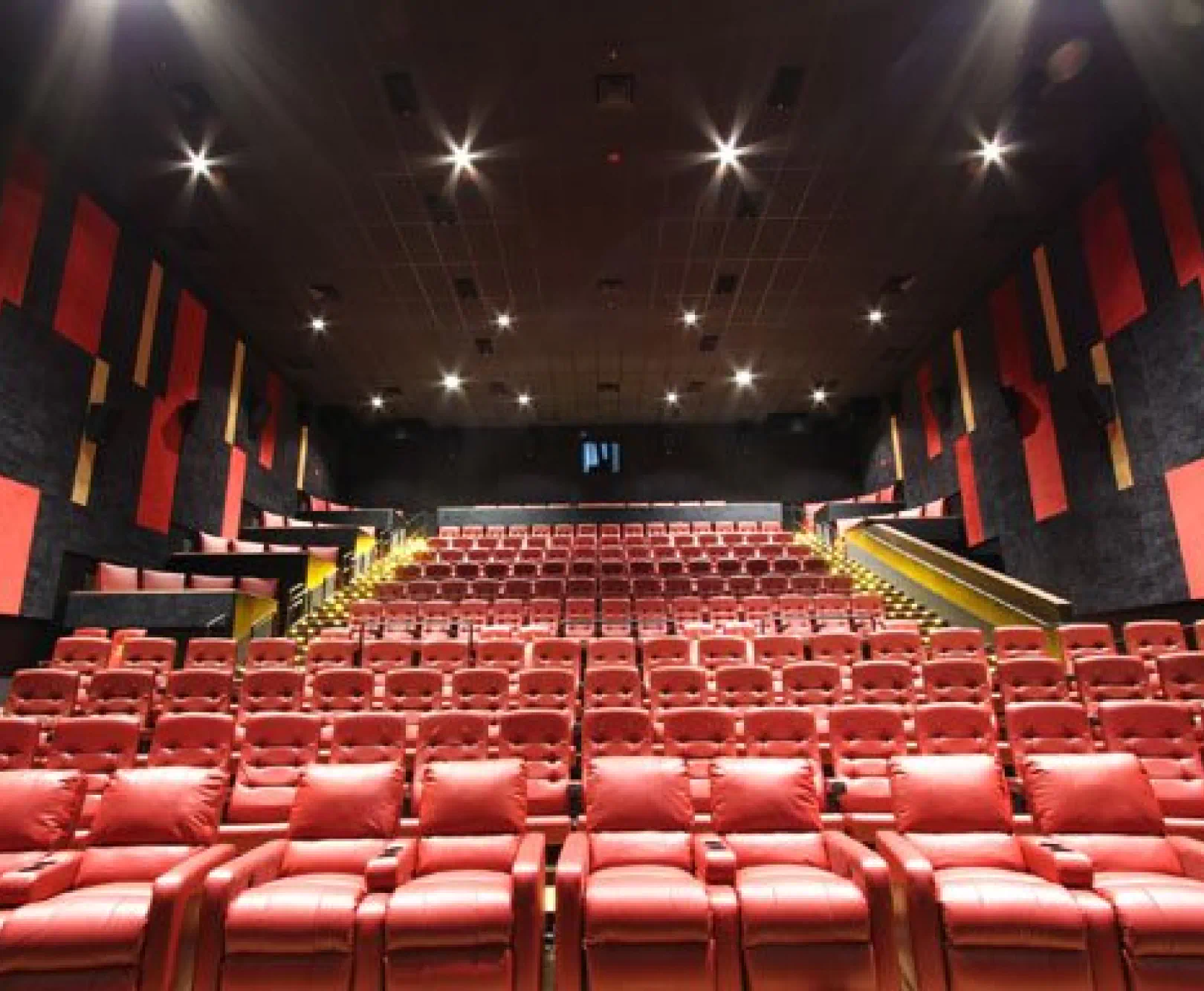 Interior of an AMC movie theater with red cushioned seats and stair aisles with yellow handrails.