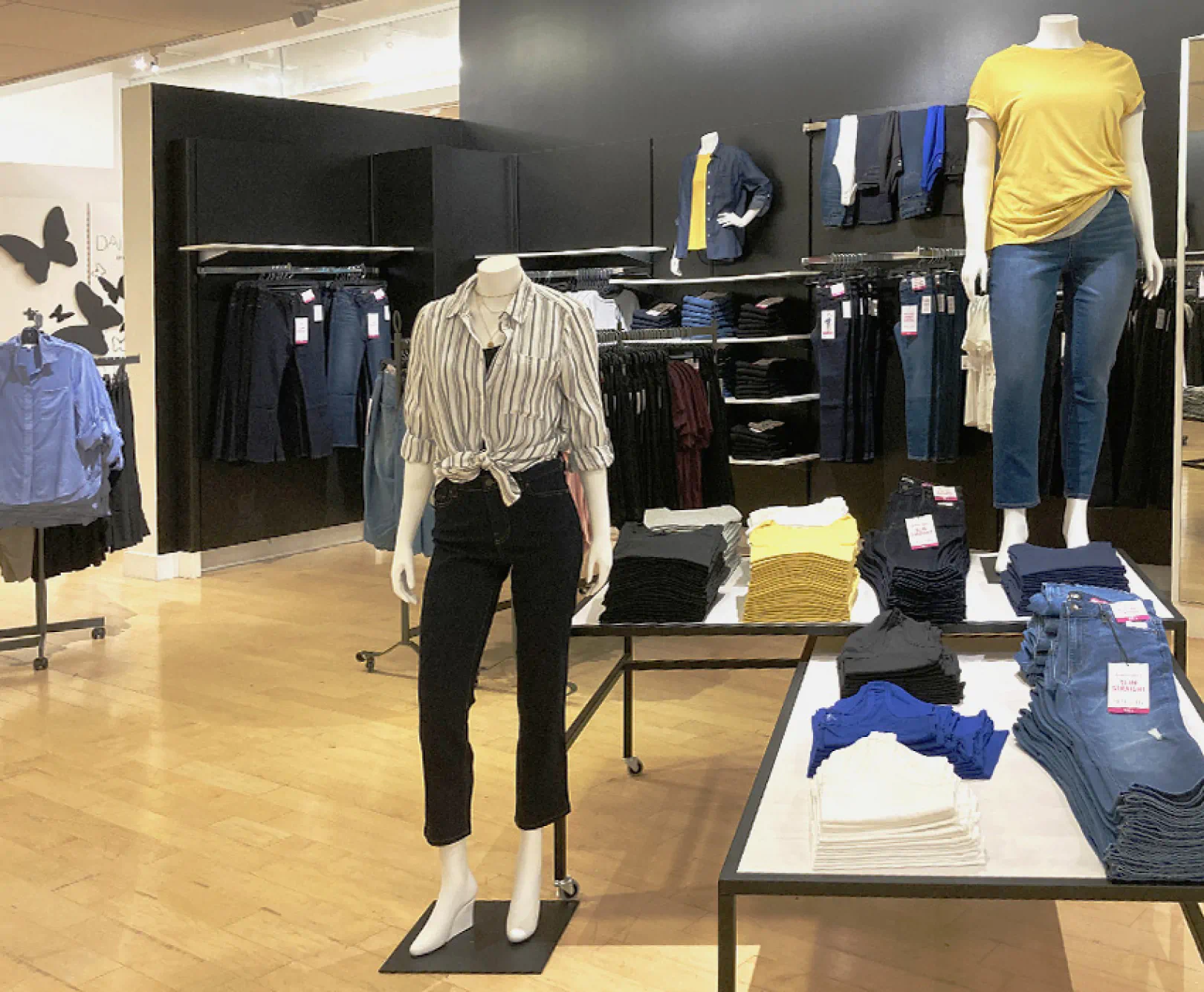 Clothing store with mannequins dressed in casual outfits and various clothes displayed on shelves and tables.