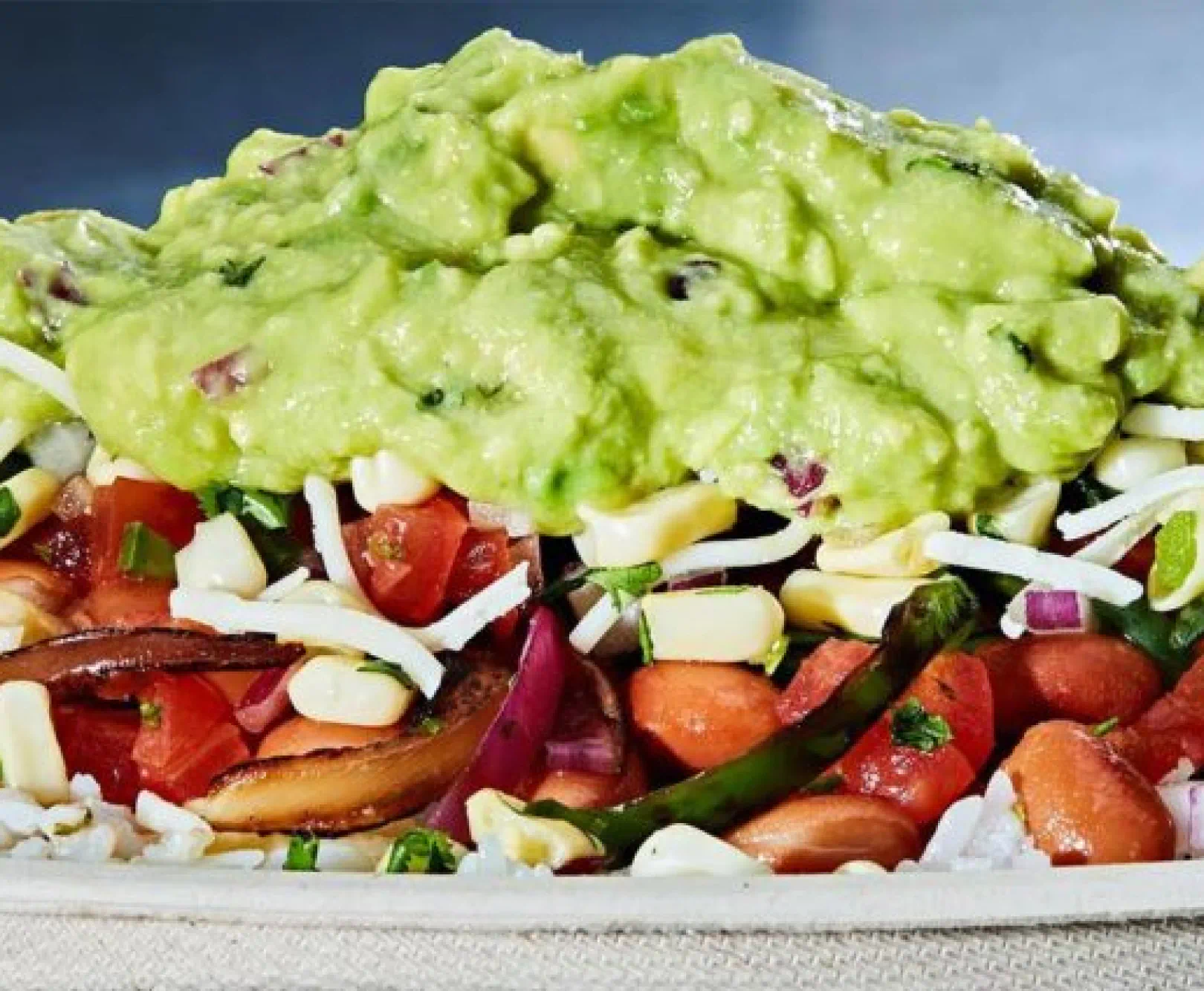 a Chipotle bowl featuring layers of rice, pico de gallo, cheese, corn, and guacamole