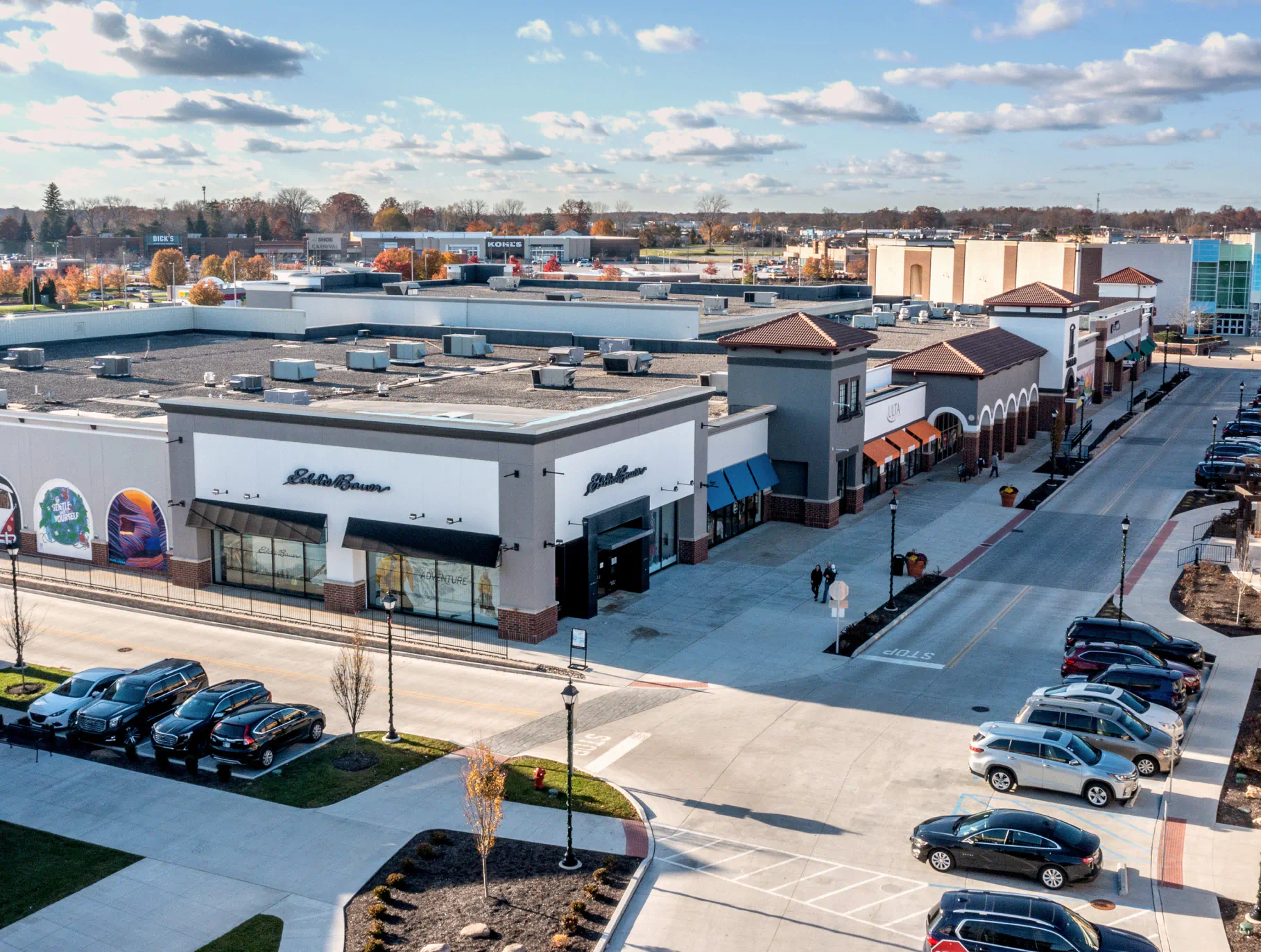 Aerial view of Jefferson Pointe shopping center with cars parked along a pedestrian-friendly street, retail stores, and an AMC theater in the distance.