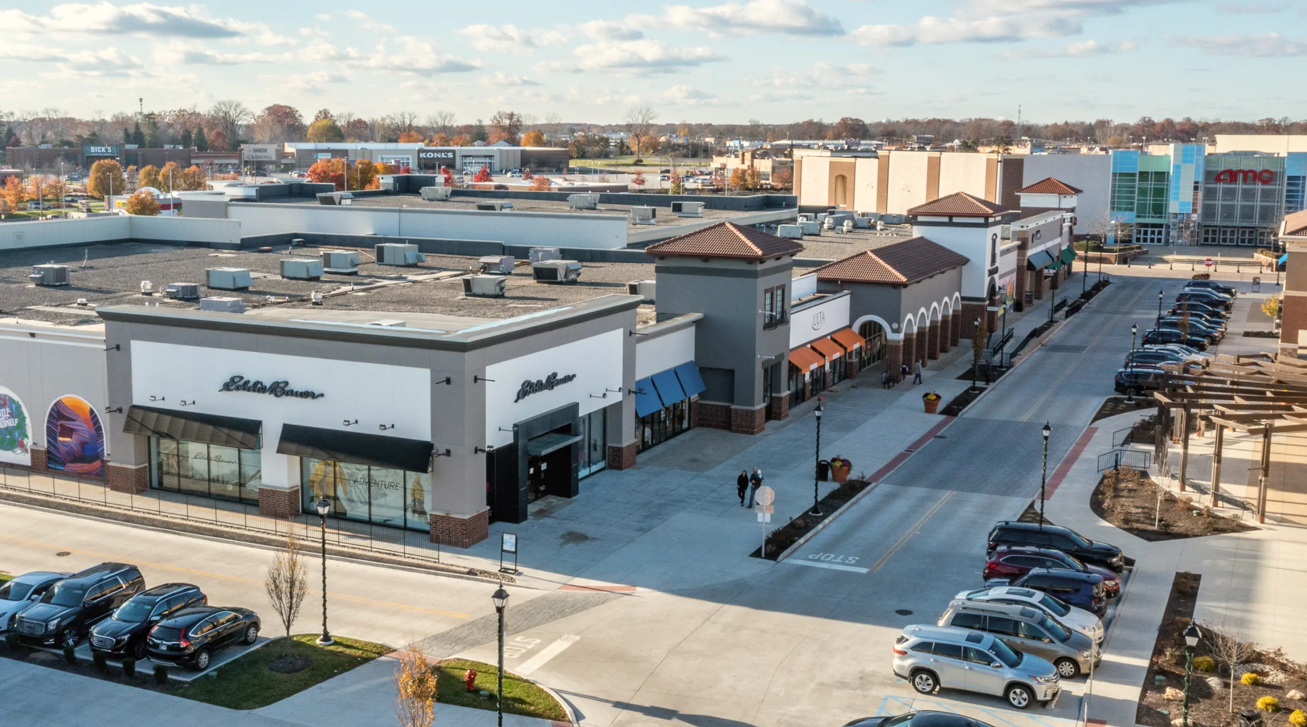 Aerial view of Jefferson Pointe shopping center with stores, including "Eddie Bauer" and "LOFT," parked cars, sidewalks, and a small landscaped area.