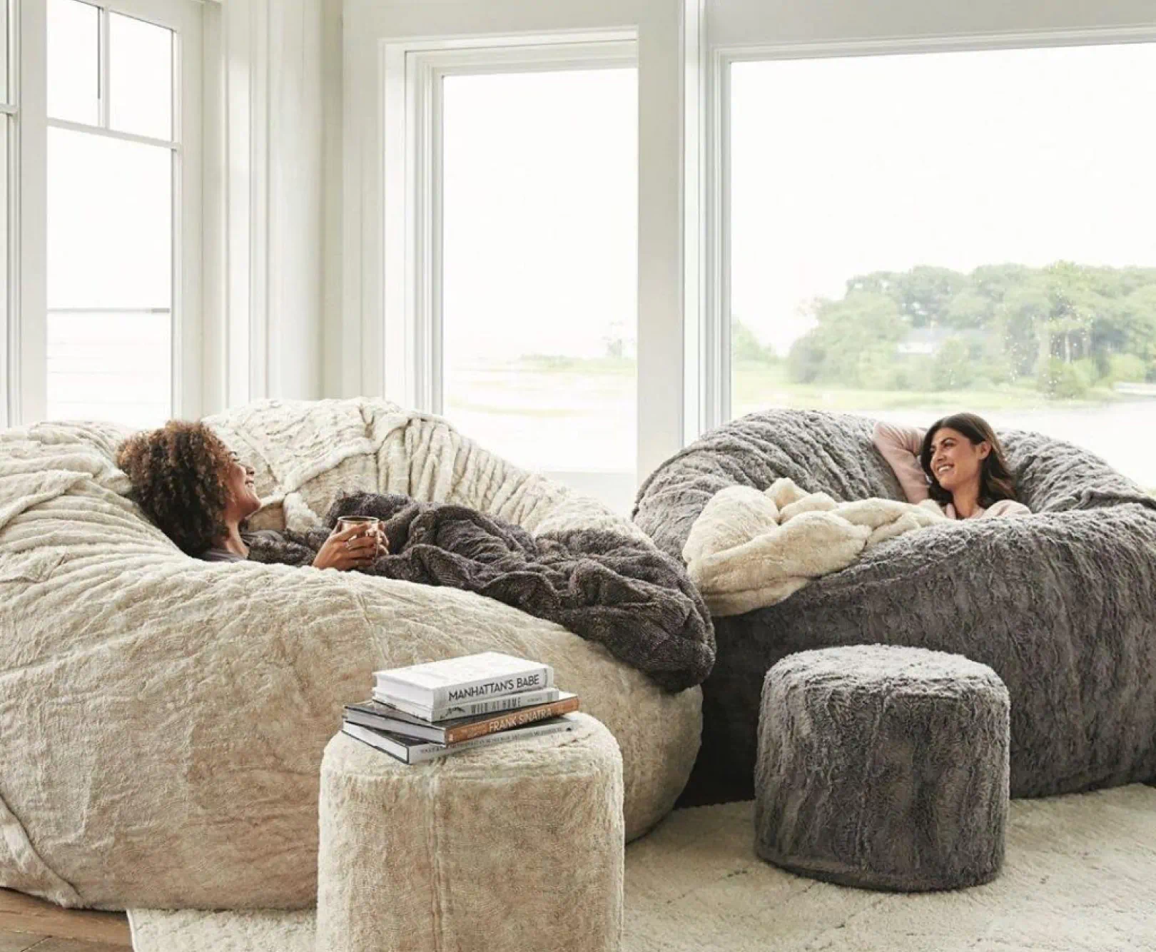 Two people lounging on oversized, plush bean bags, Lovesacs, in a bright room with large windows.