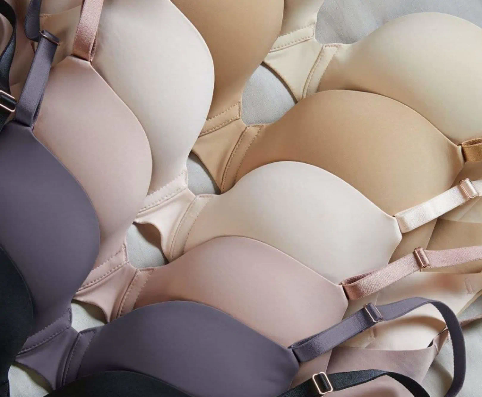 Assorted bras in shades of beige, pink, and gray, arranged in overlapping rows.