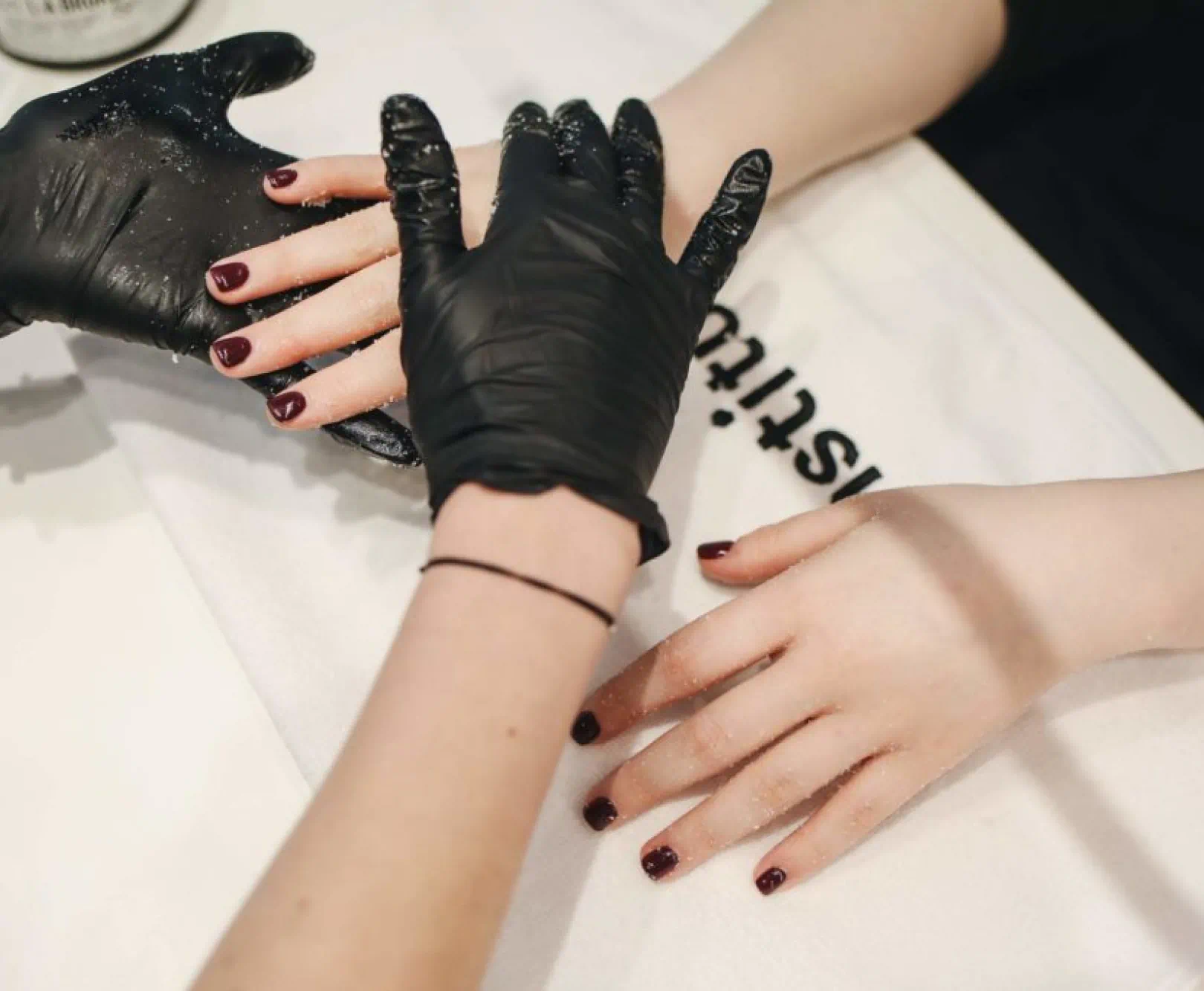 A person wearing black gloves is giving another person a manicure on a white towel