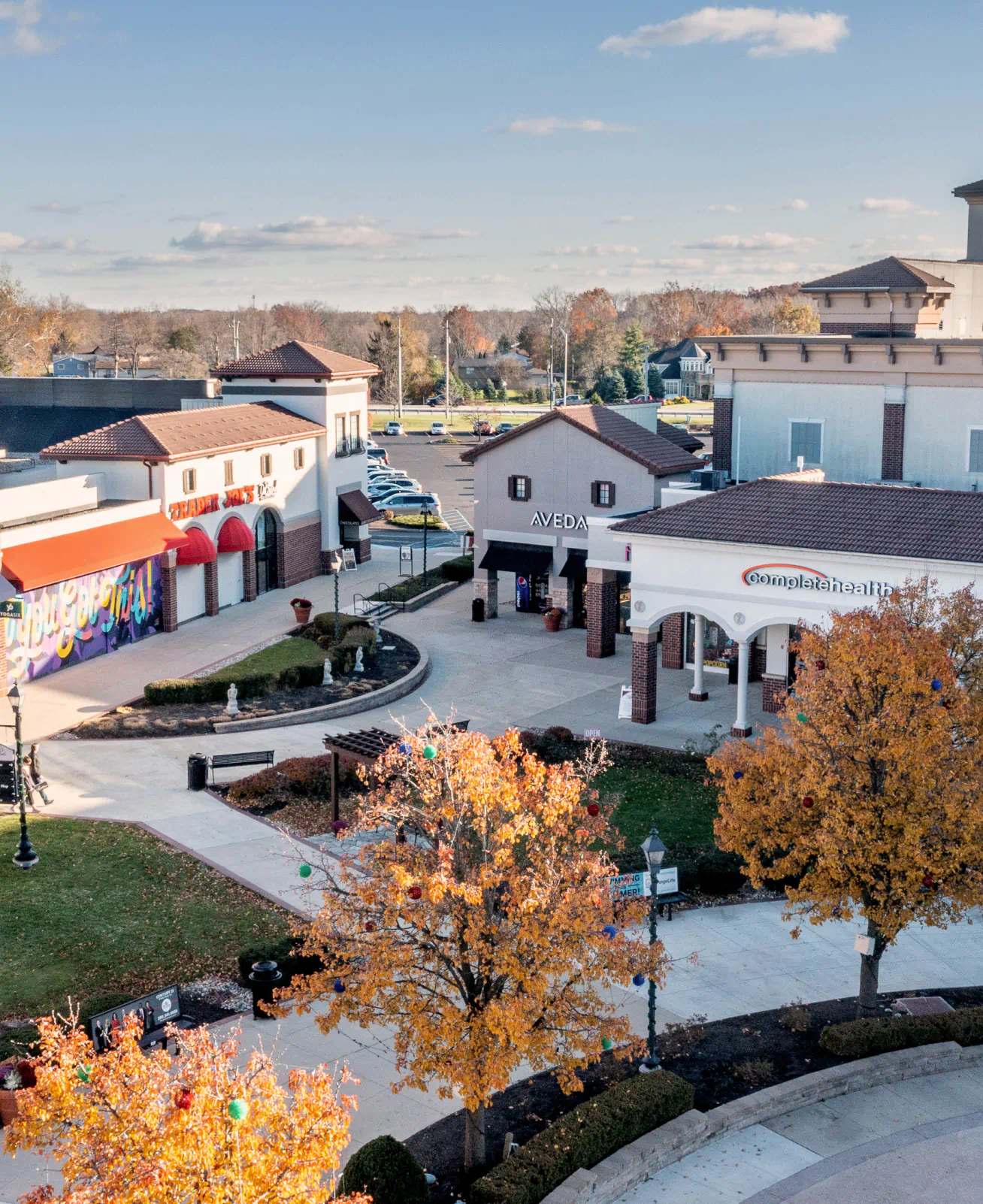 Storefronts in the Jefferson Pointe shopping center, small community area with trees and grass, storefronts including "Trader Joe's", "Aveda", and "Complete Health".