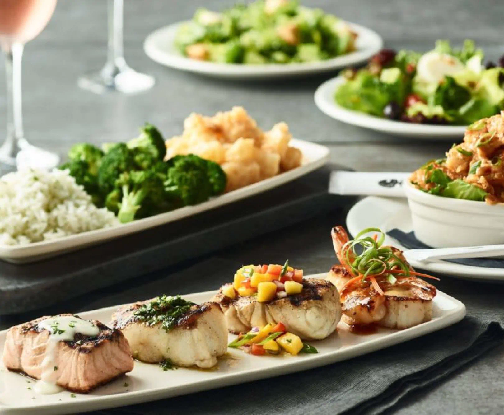 Pieces of fish and plates of vegetables sit on a gray table.