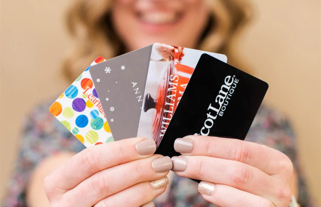 A woman with painted nails holds up four gift cards.