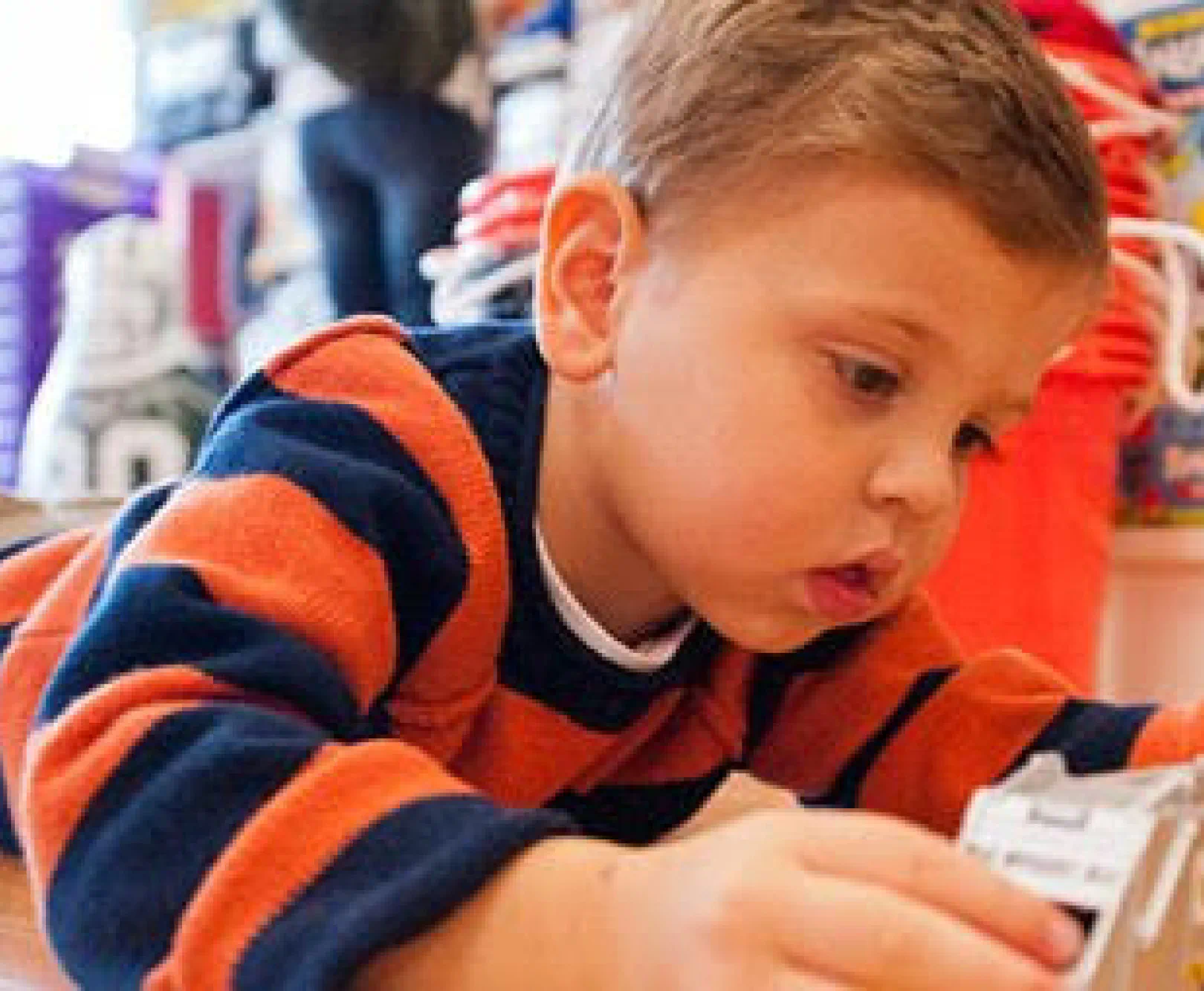 A small child in an orange and blue sweater plays with a toy.