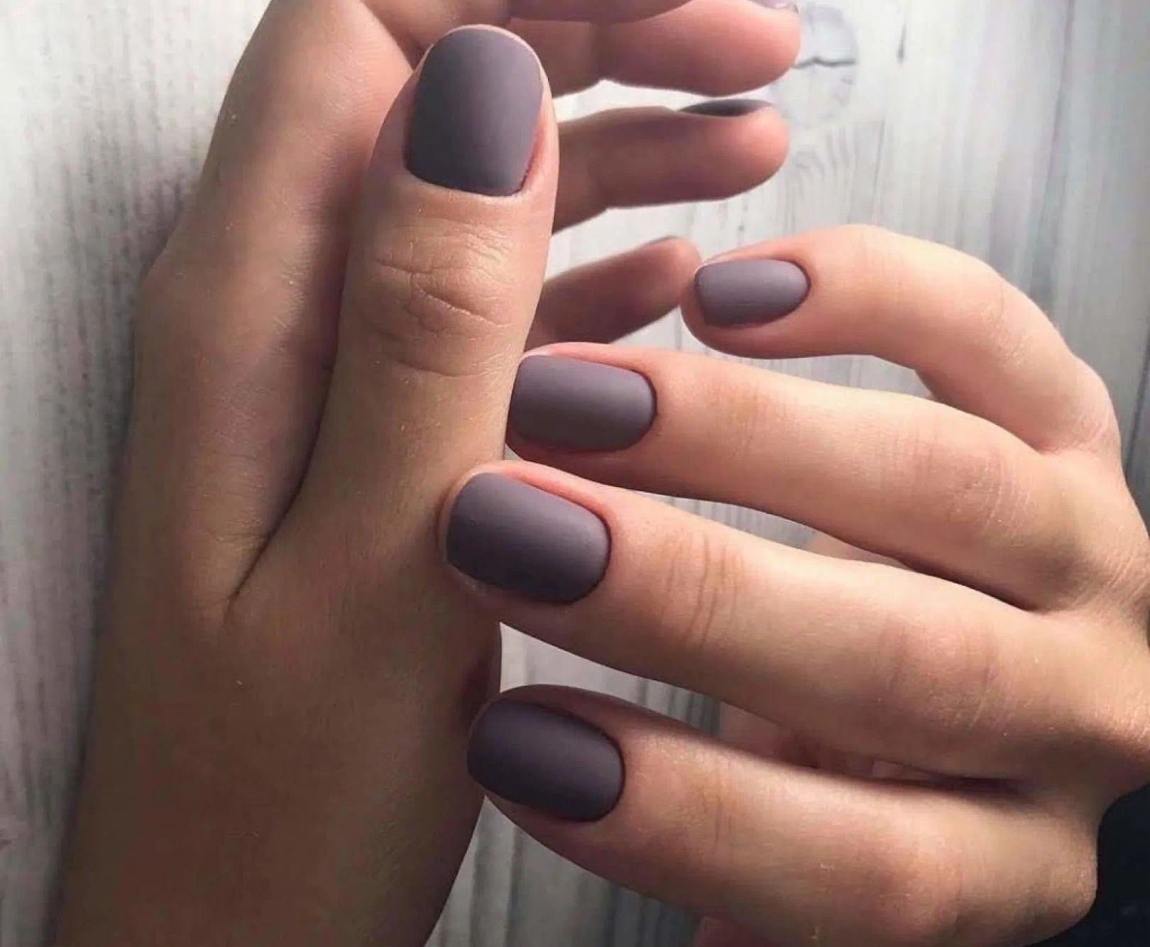 A close up of hands with perfectly manicured purple nails.