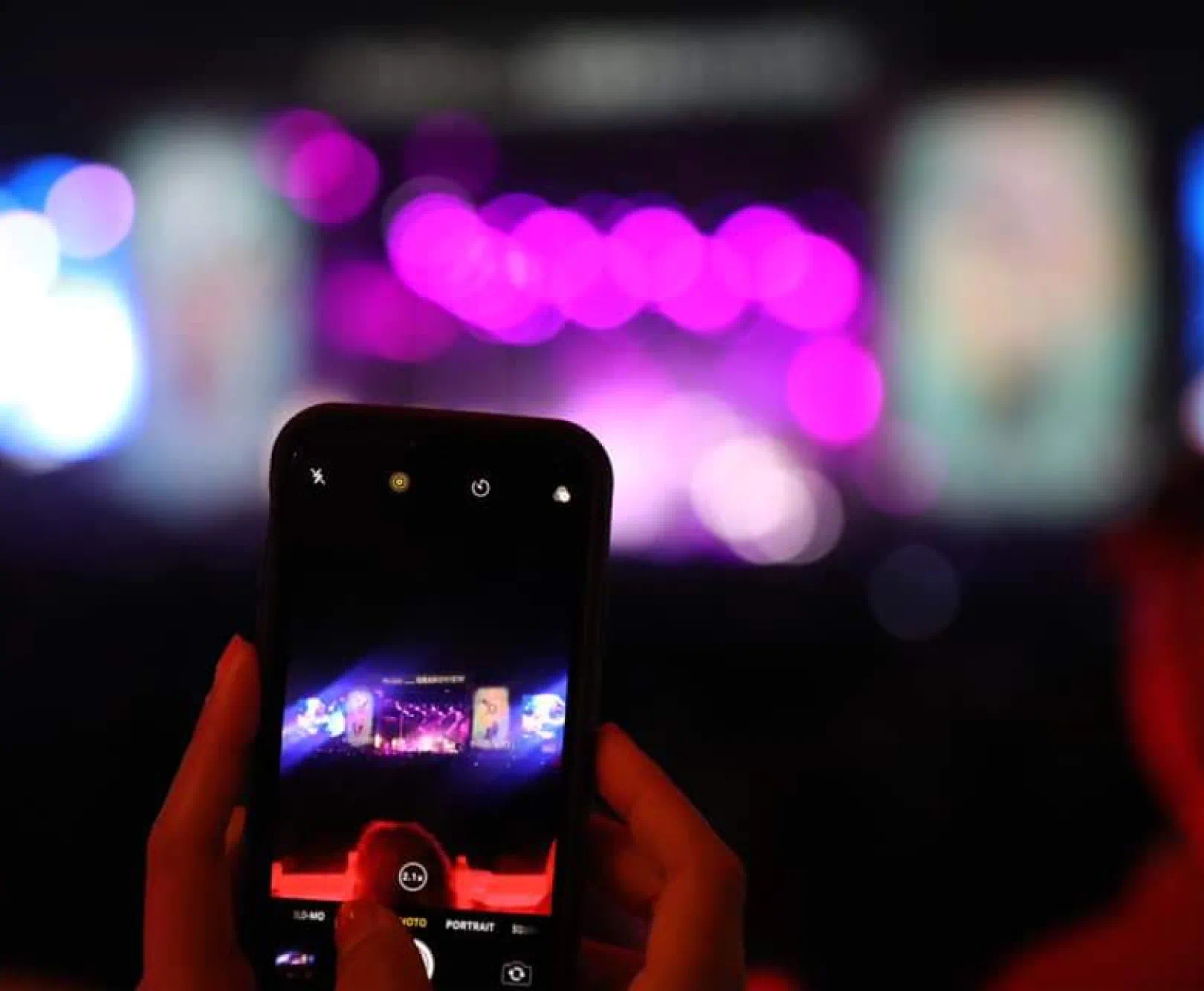 A person filming a band on a stage on their phone