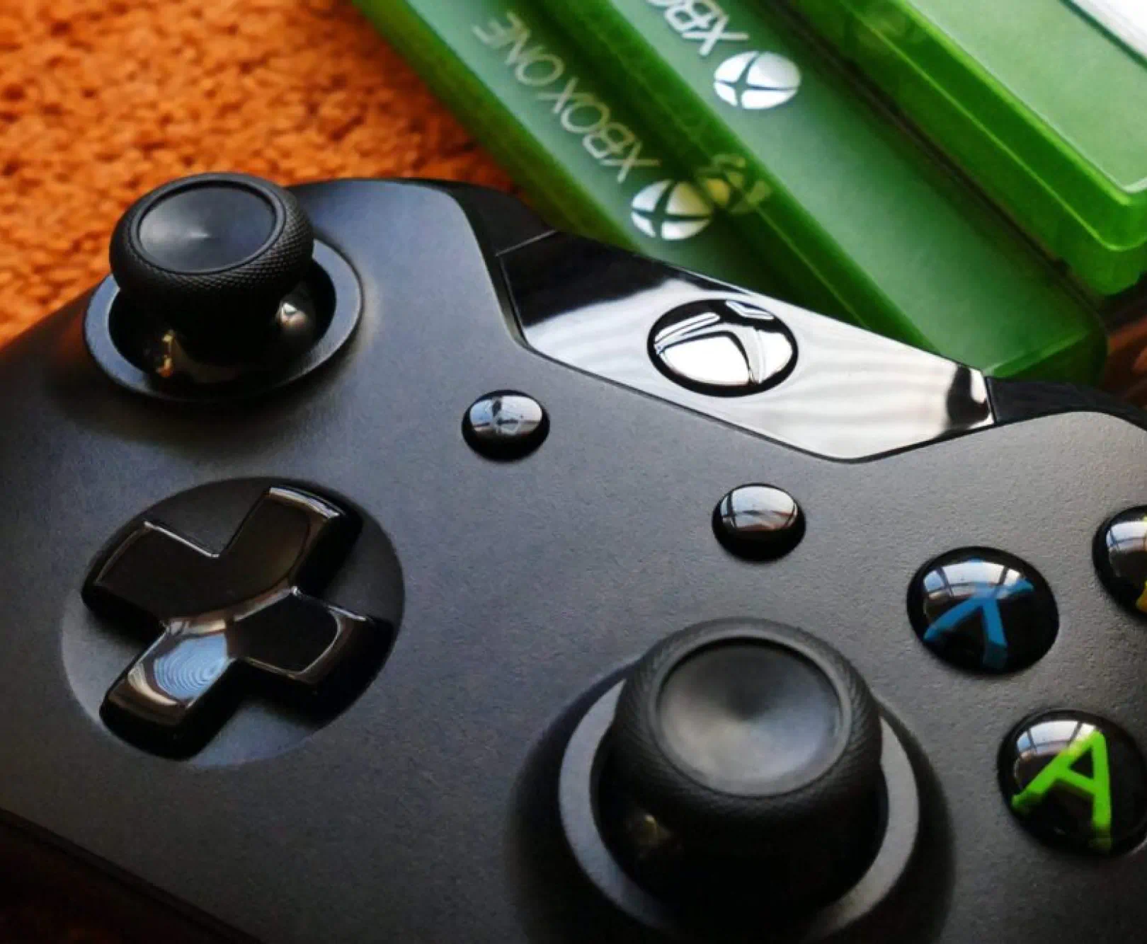 an xbox one controller sits on an orange carpet with three xbox one games sitting beside it