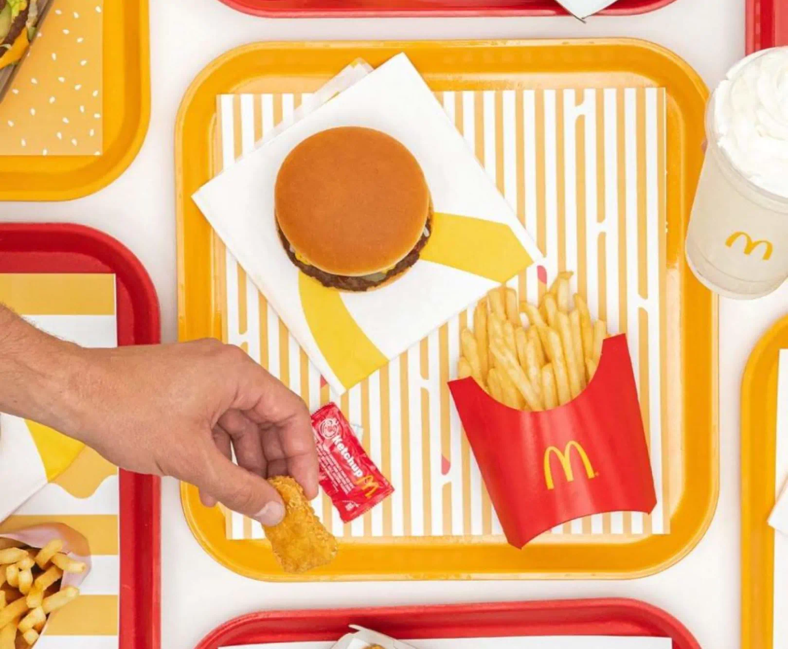 Top-down view of a fast-food meal with a hamburger, French fries, and hash brown on a yellow tray.