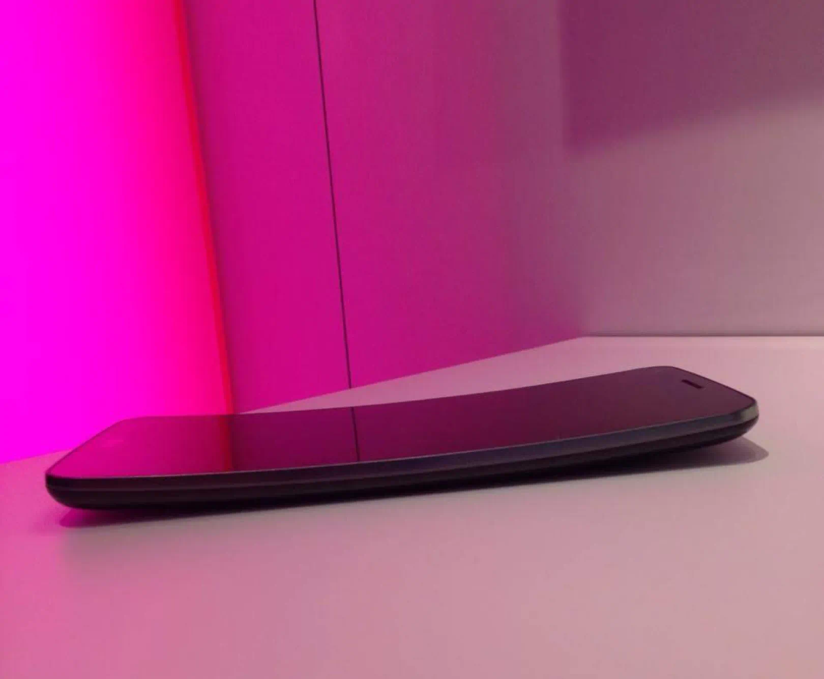 a smart phone sitting on a white surface with pink ambient lighting