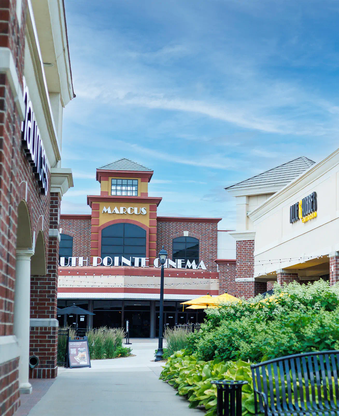 View of the outdoor pavilion at South Pointe, store fronts line the walkway with a bench and landscaping. A cinema sits at the end of the open space.