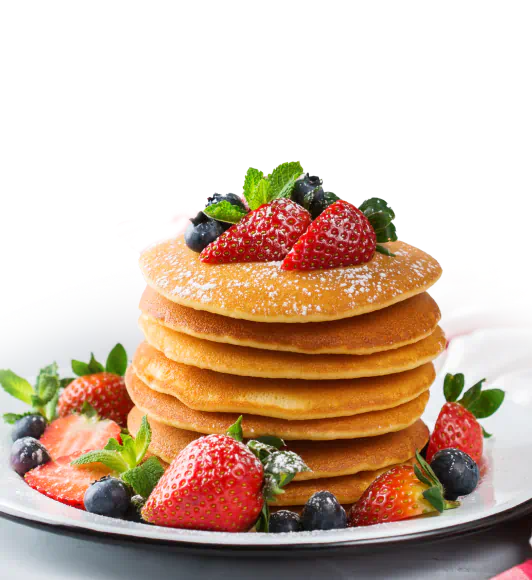 Stack of pancakes adorned with strawberries, blueberries, and powdered sugar on a white plate.