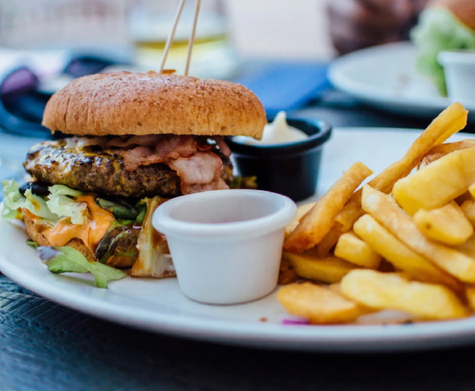 A hamburger and fires sit on a white plate served with mayo.