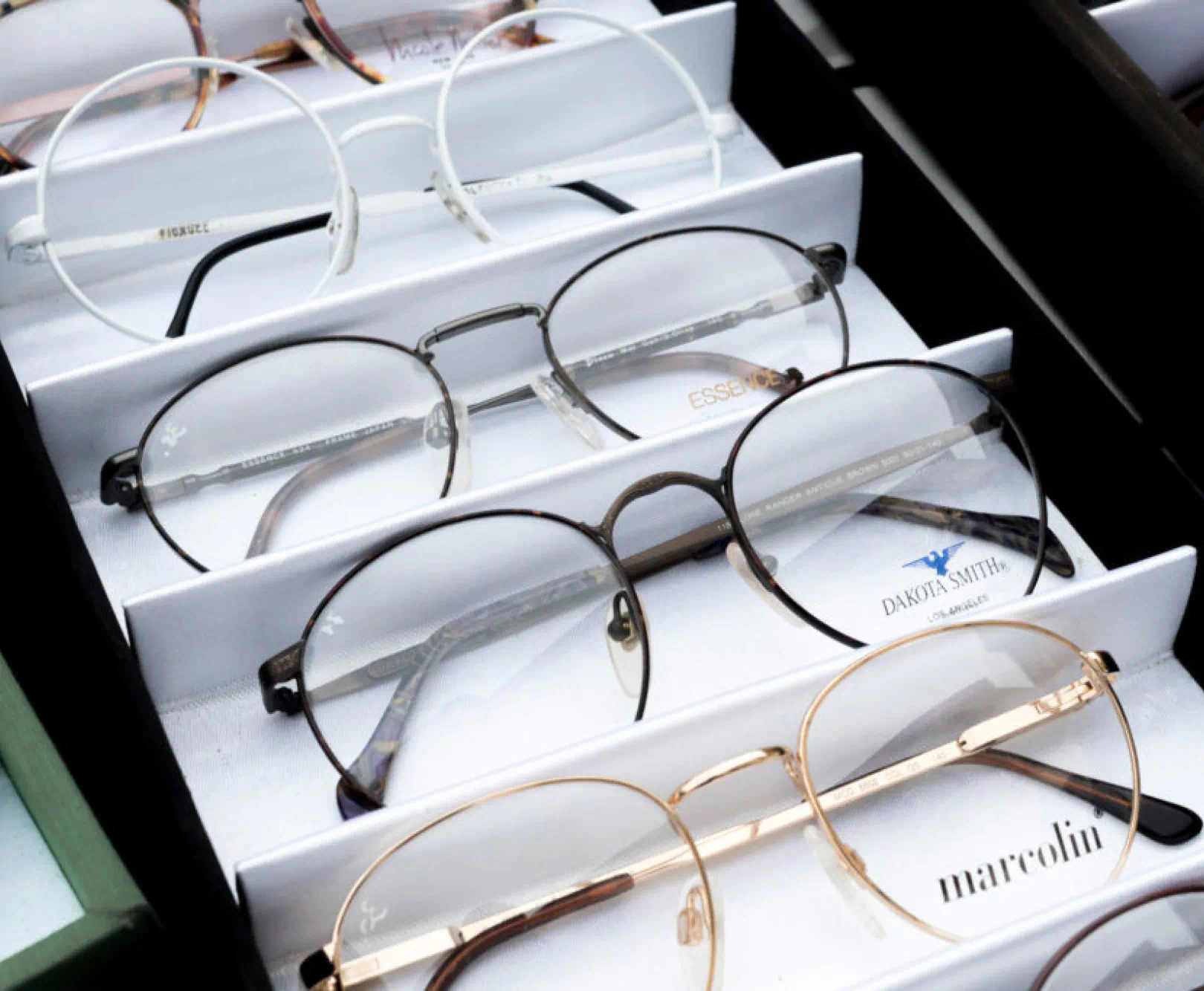 A collection of glasses sit in a display. Each features tin, metal frames in an assortment of colors.