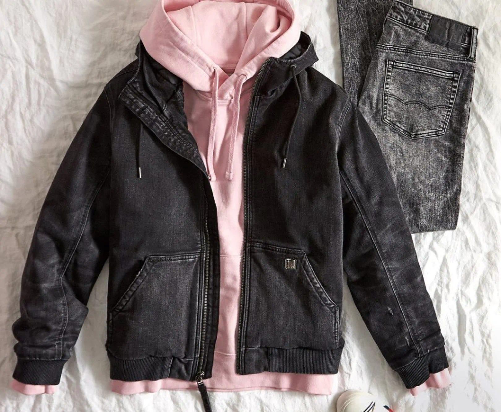 A black denim coat and pink hoodie sit atop a crushed white linen tablecloth.