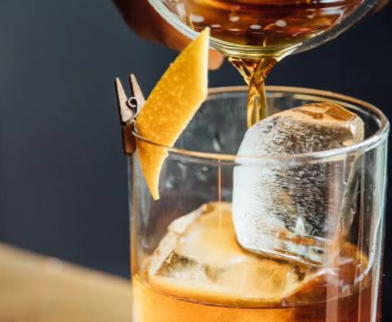 A bartender pours an Old Fashioned over crystal clear ice cubes.