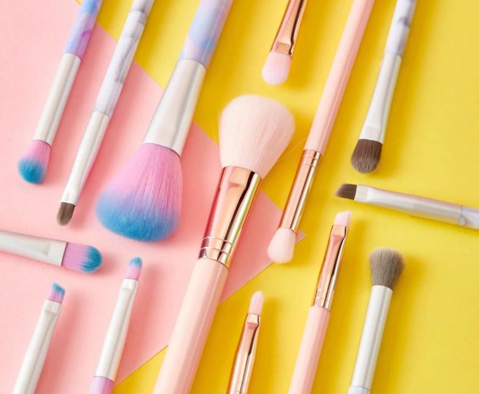 A collection of pink makeup brushes sit on a yellow and pink surface.