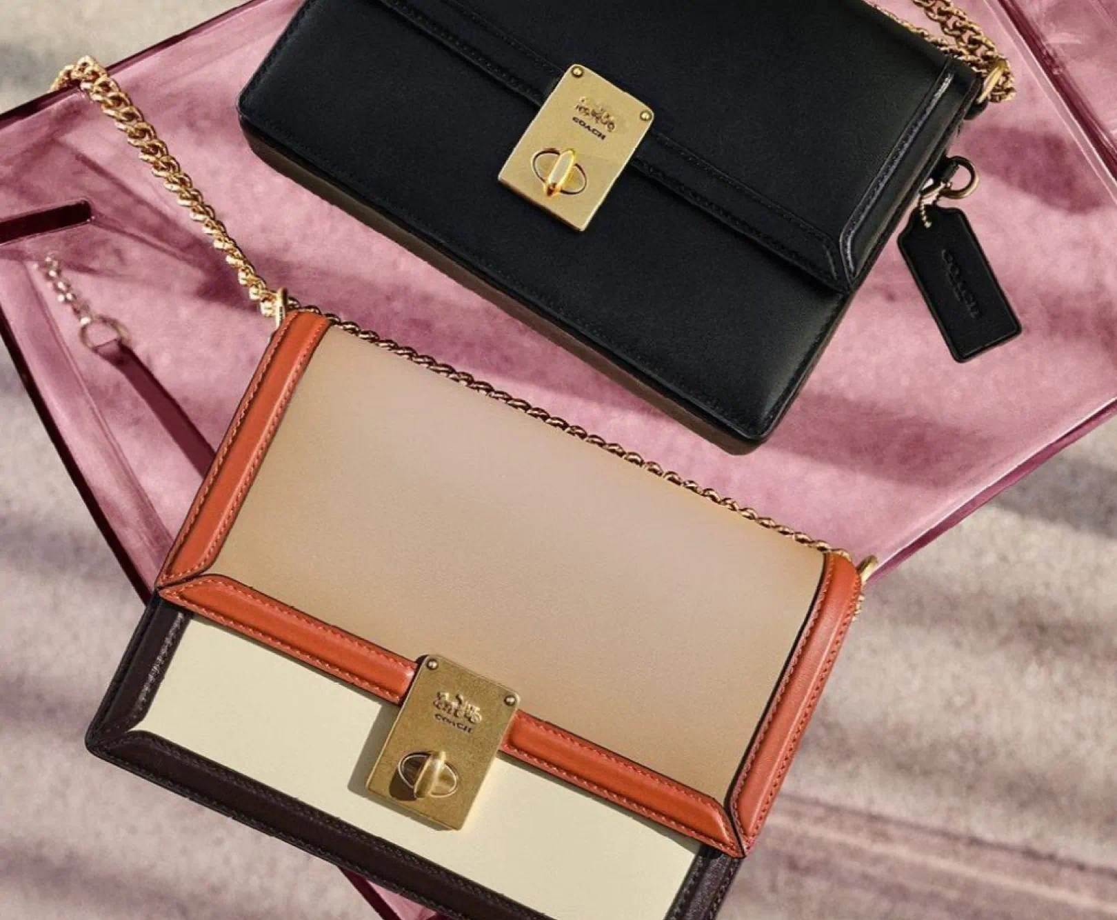 Two Coach purses, one black and one tan, sit on a pink satin cloth.