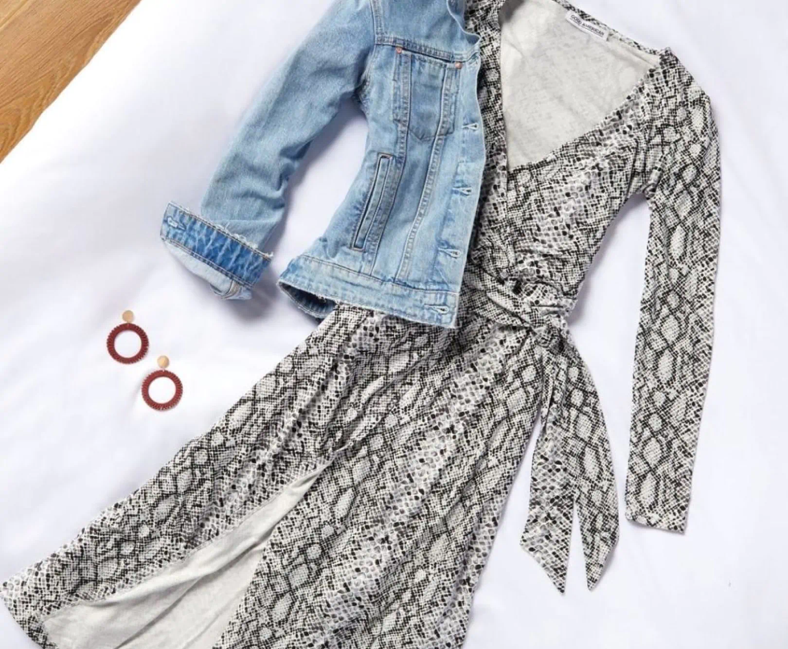 A dress with a snakeskin pattern and denim coat sit on a white cloth.