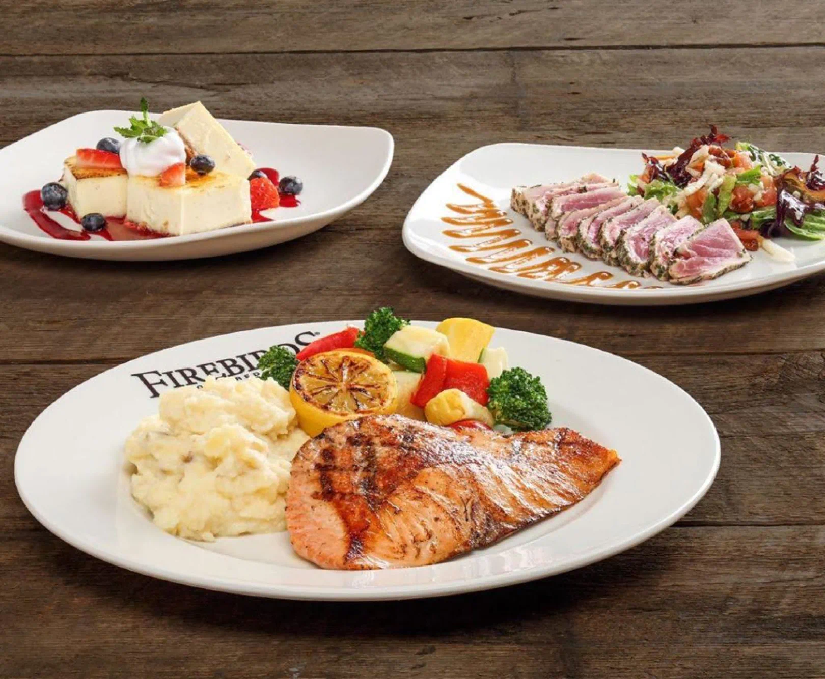 A grilled salmon, seared ahi tuna and cheesecake sit on three Firebird's dinner plates.