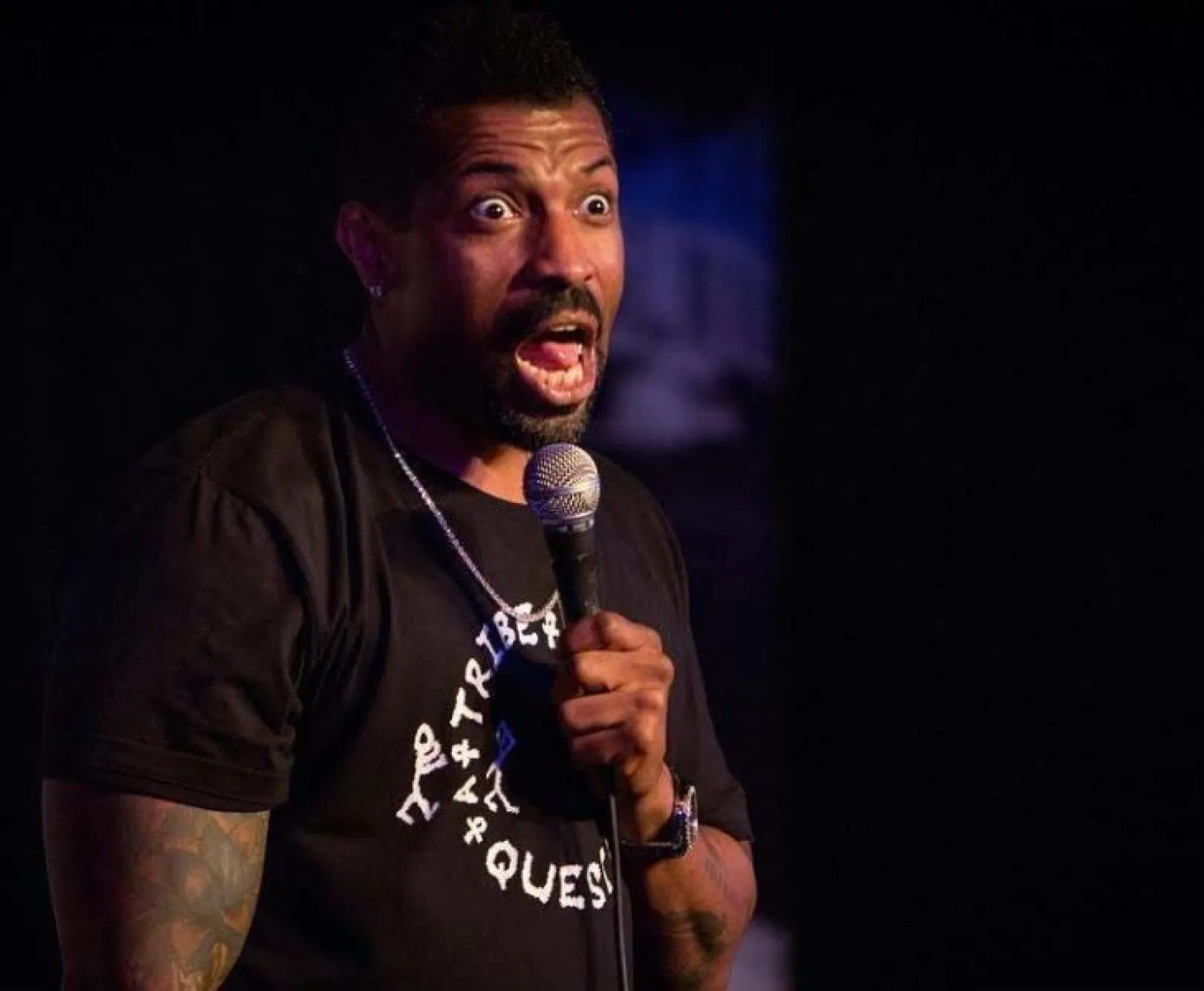 Deon Cole performs at the Funny Bone Comedy club in black t-shirt.