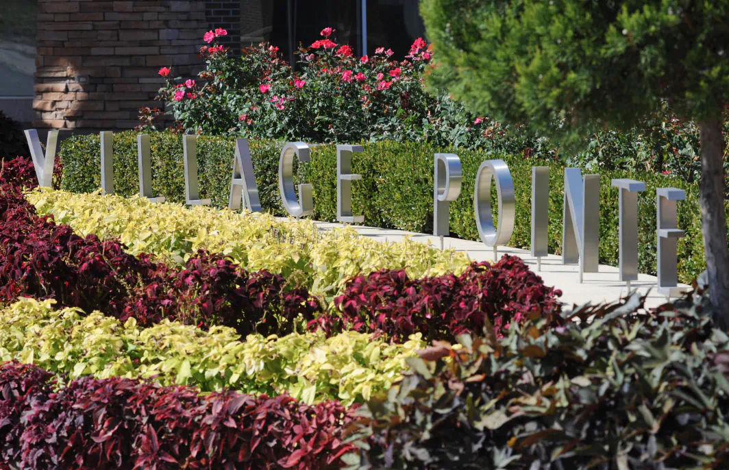 Red, yellow, pink, and green plants surround a brushed metal sculpture of letters spelling out Village Pointe.