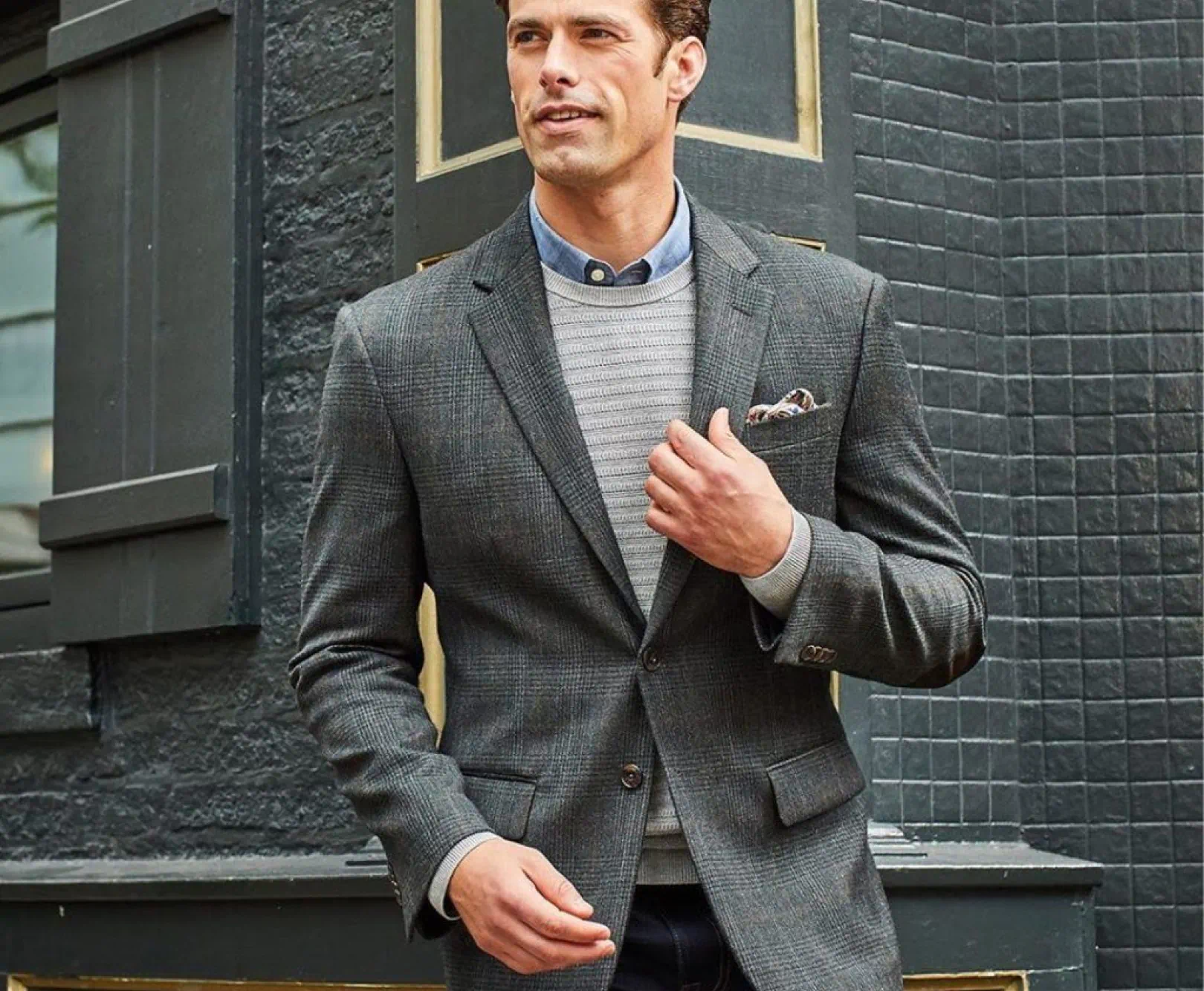 A sharply dressed man in a grey blazer adjusts his lapel.