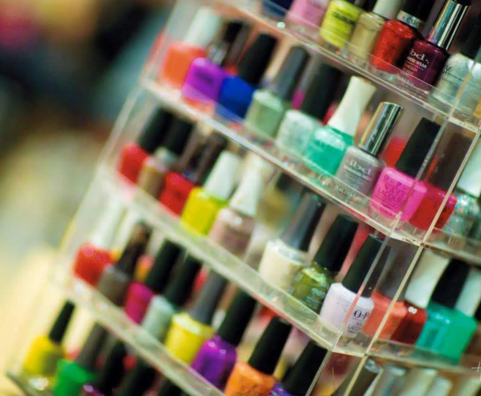 A collection of colorful nail polishes sit in an acrylic stand.